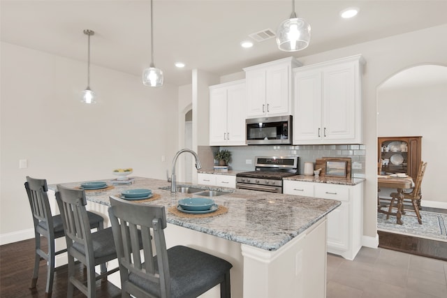 kitchen featuring a kitchen island with sink, pendant lighting, sink, white cabinets, and appliances with stainless steel finishes