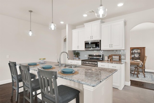 kitchen featuring an island with sink, sink, stainless steel dishwasher, a stone fireplace, and white cabinetry