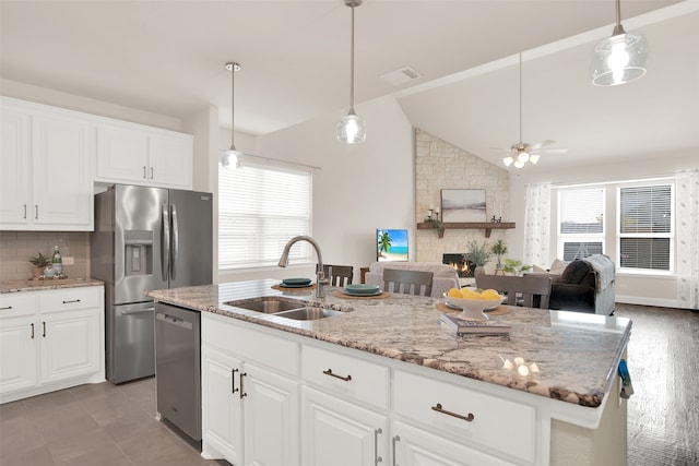 kitchen featuring white cabinets, an island with sink, sink, a stone fireplace, and stainless steel appliances