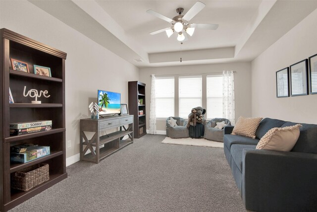 living room featuring ceiling fan, a raised ceiling, and dark colored carpet