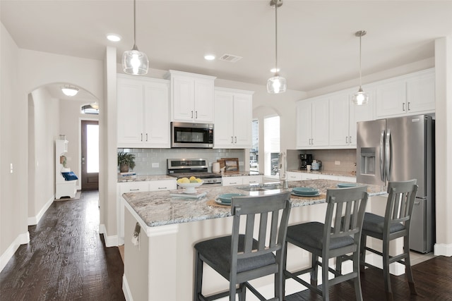 kitchen with appliances with stainless steel finishes, hanging light fixtures, a center island with sink, and white cabinets