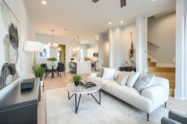 living room featuring ceiling fan with notable chandelier, light wood-type flooring, and sink