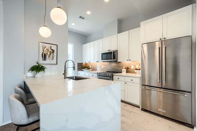 kitchen with sink, appliances with stainless steel finishes, decorative light fixtures, light stone counters, and kitchen peninsula