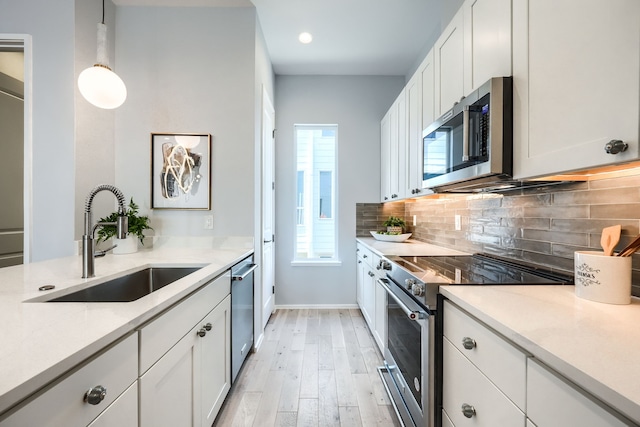 kitchen featuring white cabinetry, sink, stainless steel appliances, and decorative light fixtures