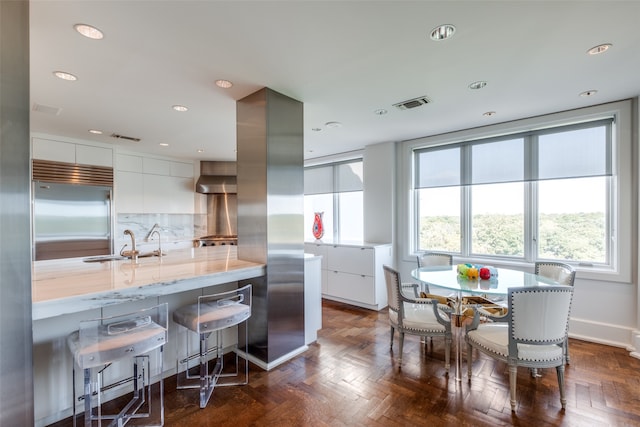 kitchen featuring light stone counters, white cabinets, sink, stainless steel built in refrigerator, and backsplash