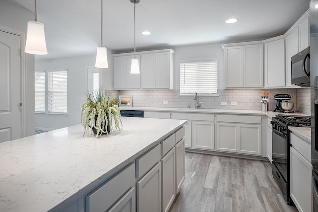 kitchen featuring sink, black appliances, a center island, white cabinetry, and hanging light fixtures