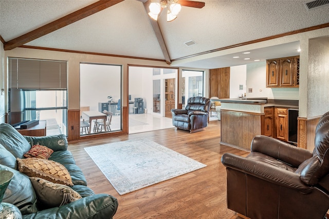 living room with ceiling fan, crown molding, light hardwood / wood-style flooring, vaulted ceiling with beams, and a textured ceiling