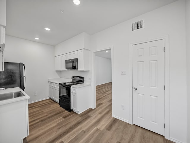 kitchen with sink, black appliances, white cabinetry, and light wood-type flooring