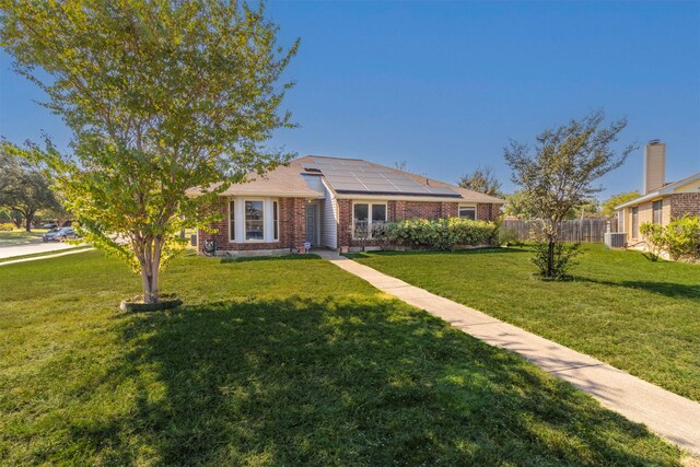 ranch-style home with a front yard, solar panels, and central air condition unit