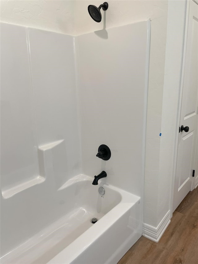 bathroom with hardwood / wood-style flooring and washtub / shower combination