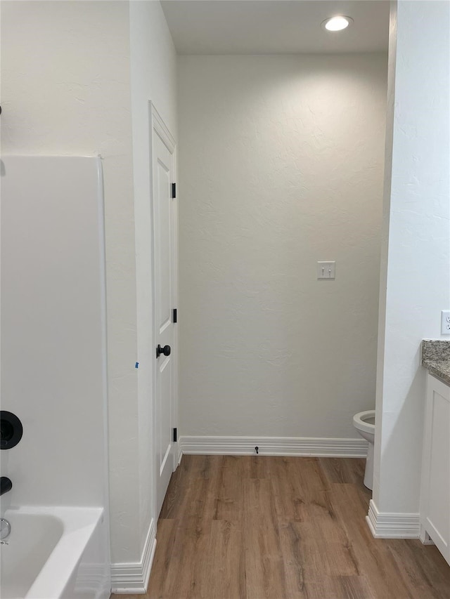 bathroom featuring wood-type flooring, vanity, toilet, and a tub