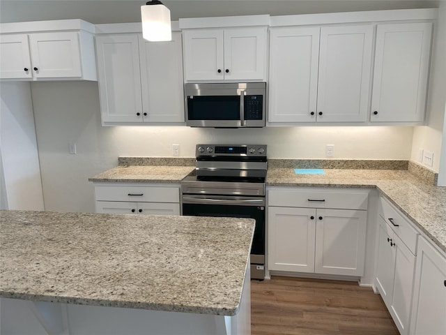 kitchen with light stone counters, white cabinets, hanging light fixtures, wood-type flooring, and stainless steel appliances