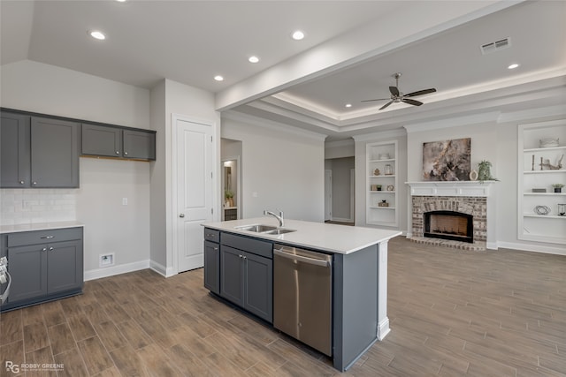 kitchen with built in shelves, stainless steel dishwasher, gray cabinetry, and an island with sink