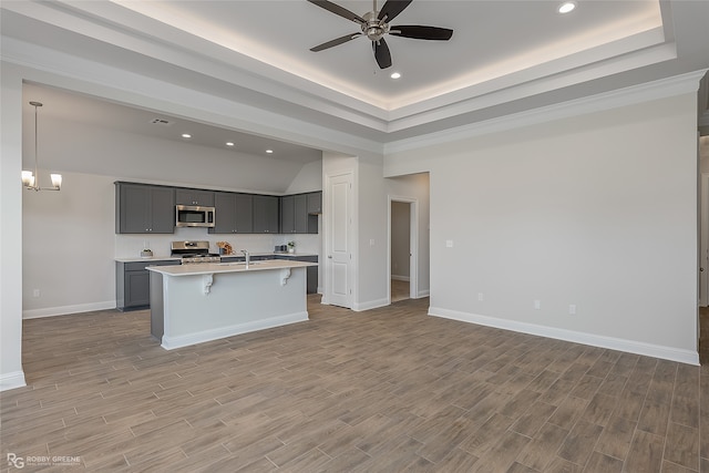 kitchen with stainless steel appliances, light hardwood / wood-style flooring, hanging light fixtures, and an island with sink