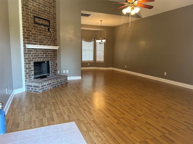 unfurnished living room with ceiling fan with notable chandelier, hardwood / wood-style flooring, a fireplace, and a textured ceiling