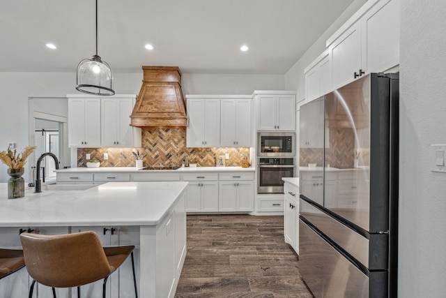 kitchen featuring pendant lighting, premium range hood, white cabinets, appliances with stainless steel finishes, and dark hardwood / wood-style flooring