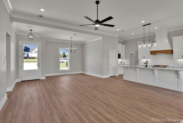 kitchen featuring light stone countertops, white cabinetry, hanging light fixtures, wood-type flooring, and a kitchen bar