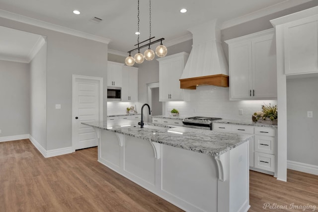 kitchen featuring white cabinetry, sink, an island with sink, custom exhaust hood, and appliances with stainless steel finishes