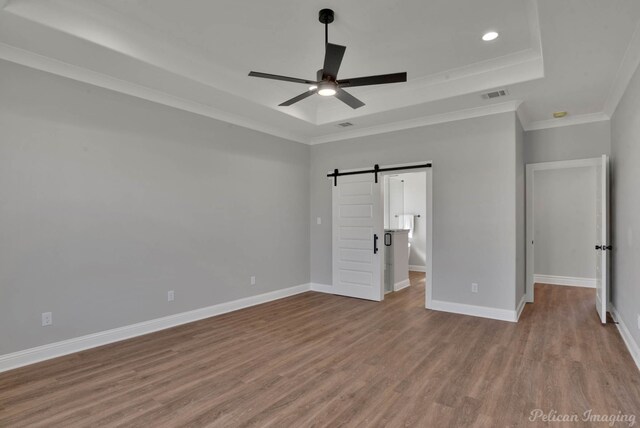 unfurnished bedroom featuring ceiling fan, a barn door, light hardwood / wood-style floors, a tray ceiling, and ornamental molding