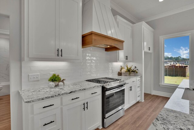 kitchen featuring ornamental molding, custom exhaust hood, stainless steel range with gas cooktop, light hardwood / wood-style flooring, and white cabinetry