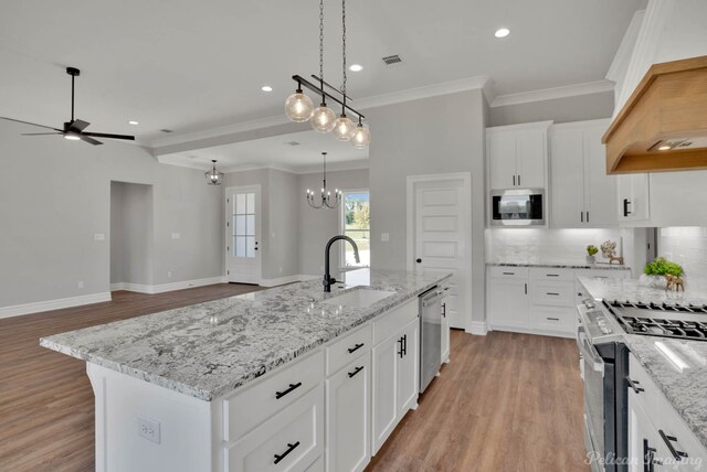 kitchen with appliances with stainless steel finishes, a kitchen island with sink, sink, light hardwood / wood-style floors, and white cabinetry