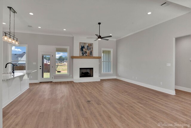 unfurnished living room with ceiling fan, a fireplace, ornamental molding, and light wood-type flooring