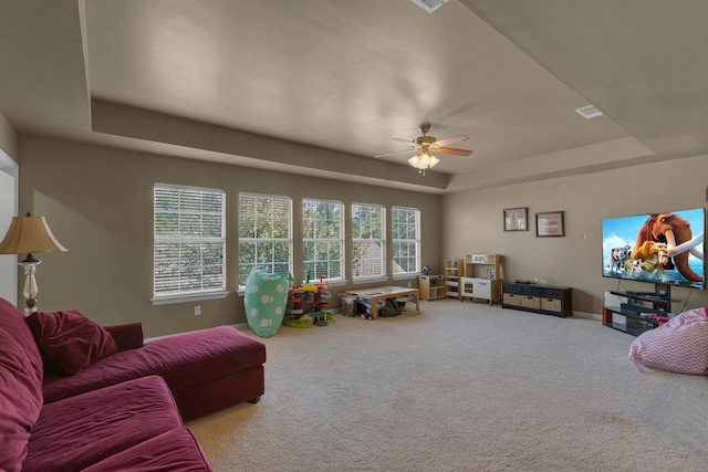 living room with ceiling fan, a tray ceiling, and carpet flooring