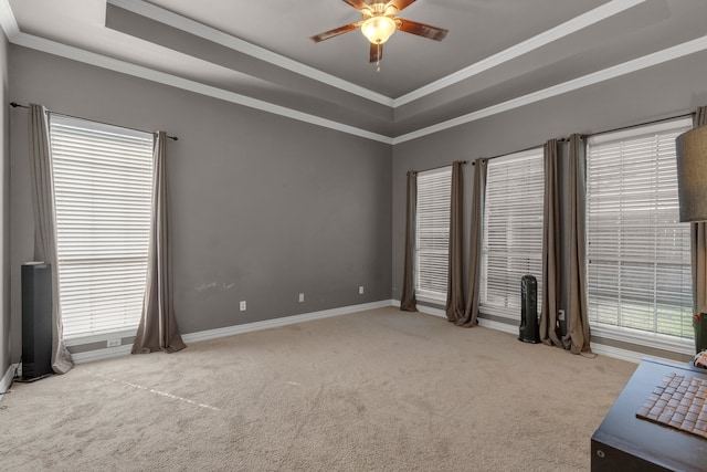 empty room featuring a raised ceiling, ceiling fan, ornamental molding, and light carpet