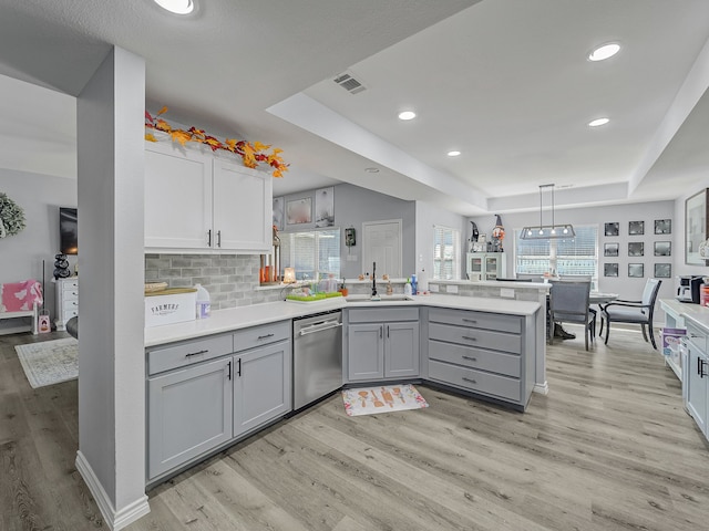 kitchen with a raised ceiling, stainless steel dishwasher, gray cabinetry, and sink