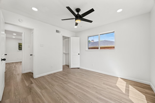 unfurnished bedroom with a closet, a walk in closet, light hardwood / wood-style flooring, and ceiling fan