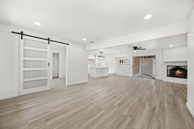 unfurnished living room featuring ceiling fan, light hardwood / wood-style flooring, a fireplace, and a barn door