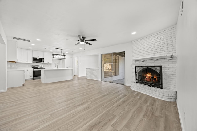 unfurnished living room featuring a brick fireplace, ceiling fan, sink, and light hardwood / wood-style floors