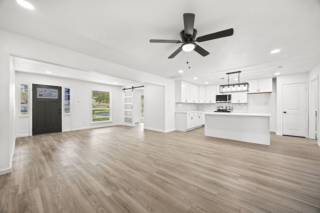 unfurnished living room featuring ceiling fan, light hardwood / wood-style floors, and a barn door