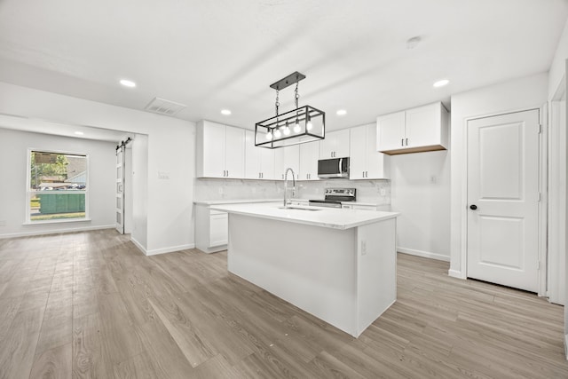 kitchen featuring appliances with stainless steel finishes, a barn door, white cabinetry, and an island with sink