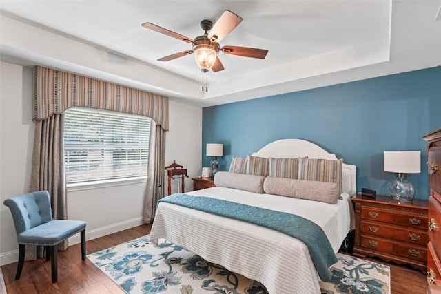 bedroom featuring ceiling fan, dark hardwood / wood-style flooring, and a tray ceiling