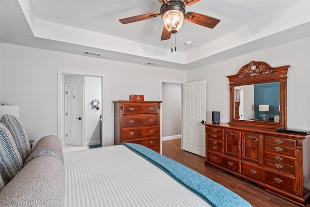 bedroom with dark wood-type flooring, ceiling fan, and a raised ceiling