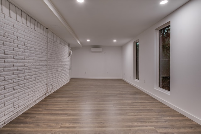 unfurnished room featuring a wall mounted AC, hardwood / wood-style flooring, and brick wall