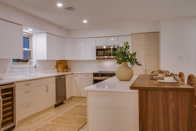 kitchen with white cabinets, wine cooler, sink, stainless steel appliances, and light wood-type flooring