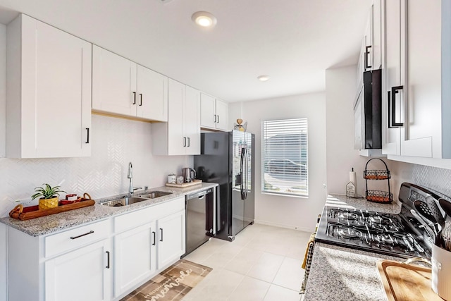 kitchen featuring light stone countertops, white cabinets, sink, appliances with stainless steel finishes, and light tile patterned floors