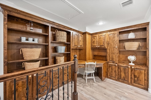 home office with light hardwood / wood-style floors, ornamental molding, and built in desk