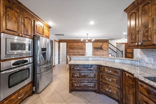 kitchen featuring kitchen peninsula, backsplash, a chandelier, appliances with stainless steel finishes, and light stone counters