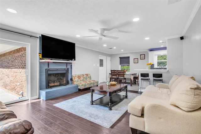 living room featuring dark wood-type flooring, a brick fireplace, crown molding, and ceiling fan