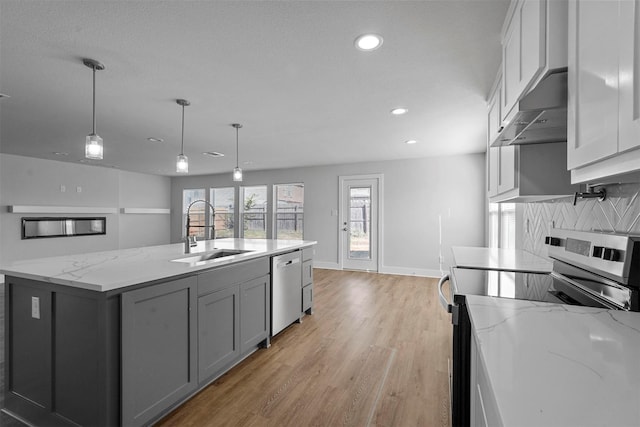 kitchen with sink, hanging light fixtures, appliances with stainless steel finishes, light stone countertops, and a kitchen island with sink