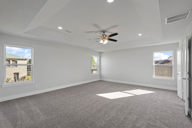 empty room featuring a raised ceiling, carpet, and ceiling fan