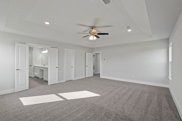 unfurnished bedroom featuring a raised ceiling, connected bathroom, and light colored carpet