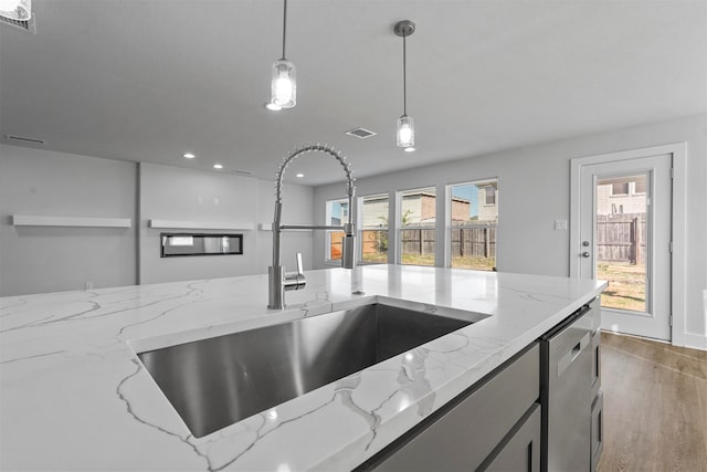 kitchen featuring light stone counters, stainless steel dishwasher, plenty of natural light, and hanging light fixtures