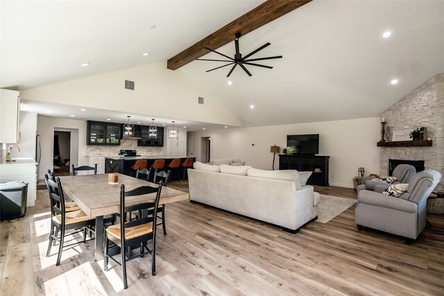 dining room with light hardwood / wood-style floors, beamed ceiling, ceiling fan, a fireplace, and high vaulted ceiling