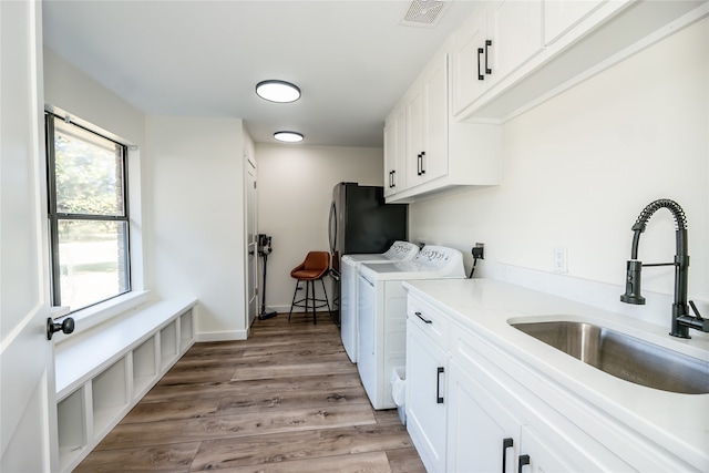 washroom featuring cabinets, washer and clothes dryer, sink, and light hardwood / wood-style flooring