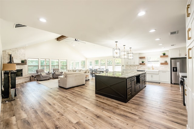 kitchen with light wood-type flooring, a kitchen island, a stone fireplace, white cabinets, and stainless steel fridge with ice dispenser