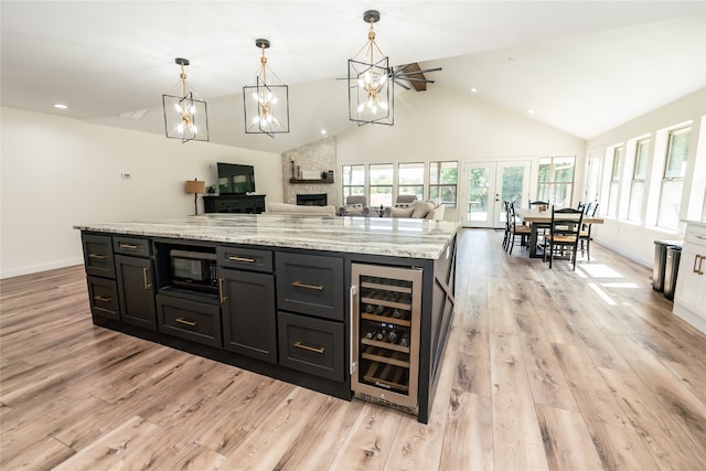 kitchen with light wood-type flooring, pendant lighting, beverage cooler, a stone fireplace, and a center island